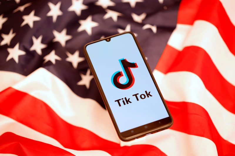 TikTok logo is displayed on the smartphone while standing on the U.S. flag