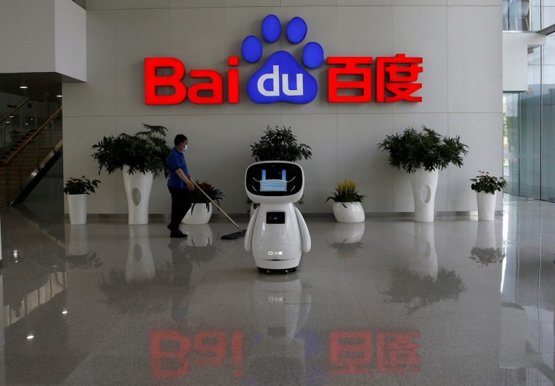 Men interact with a Baidu AI robot near the company logo at its headquarters in Beijing, China