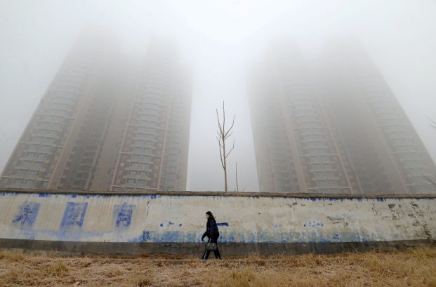 Woman wearing a mask walks past buildings on a polluted day in Hebei