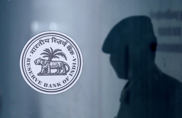 A security guard's reflection is seen next to the logo of the Reserve Bank Of India (RBI) at the RBI headquarters in Mumbai, India