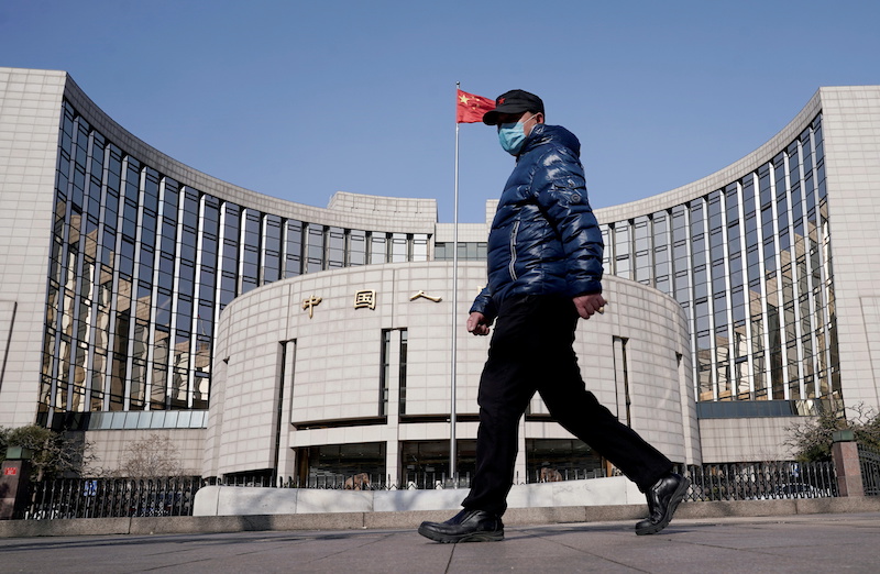 Man wearing a mask walks past the headquarters of the People's Bank of China, the central bank, in Beijing