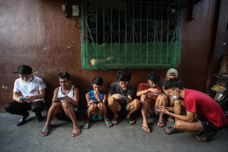 This photo taken on December 15, 2021 shows people using their mobile phones to play Axie Infinity, an NFT game where players earn tokens that can be exchanged for cryptocurrency or cash, in a neighbourhood alley in Malabon, suburban Manila. Axie Infinity is a blockchain-based play-to-earn game that exploded in popularity in developing nations such as the Philippines as Covid-19 has destroyed jobs and forced many to stay home. Jam STA ROSA / AFP