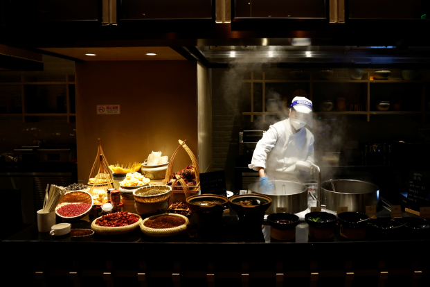 A chef wearing a mask and a face shield cooks in a restaurant