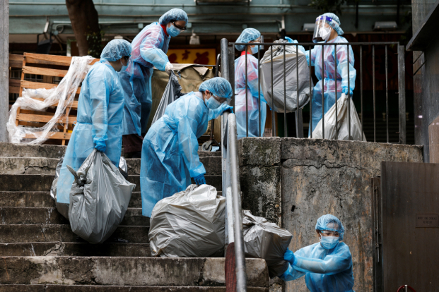 Cleaners wearing personal protective equipment (PPE) dump garbage outside a quarantine hotel