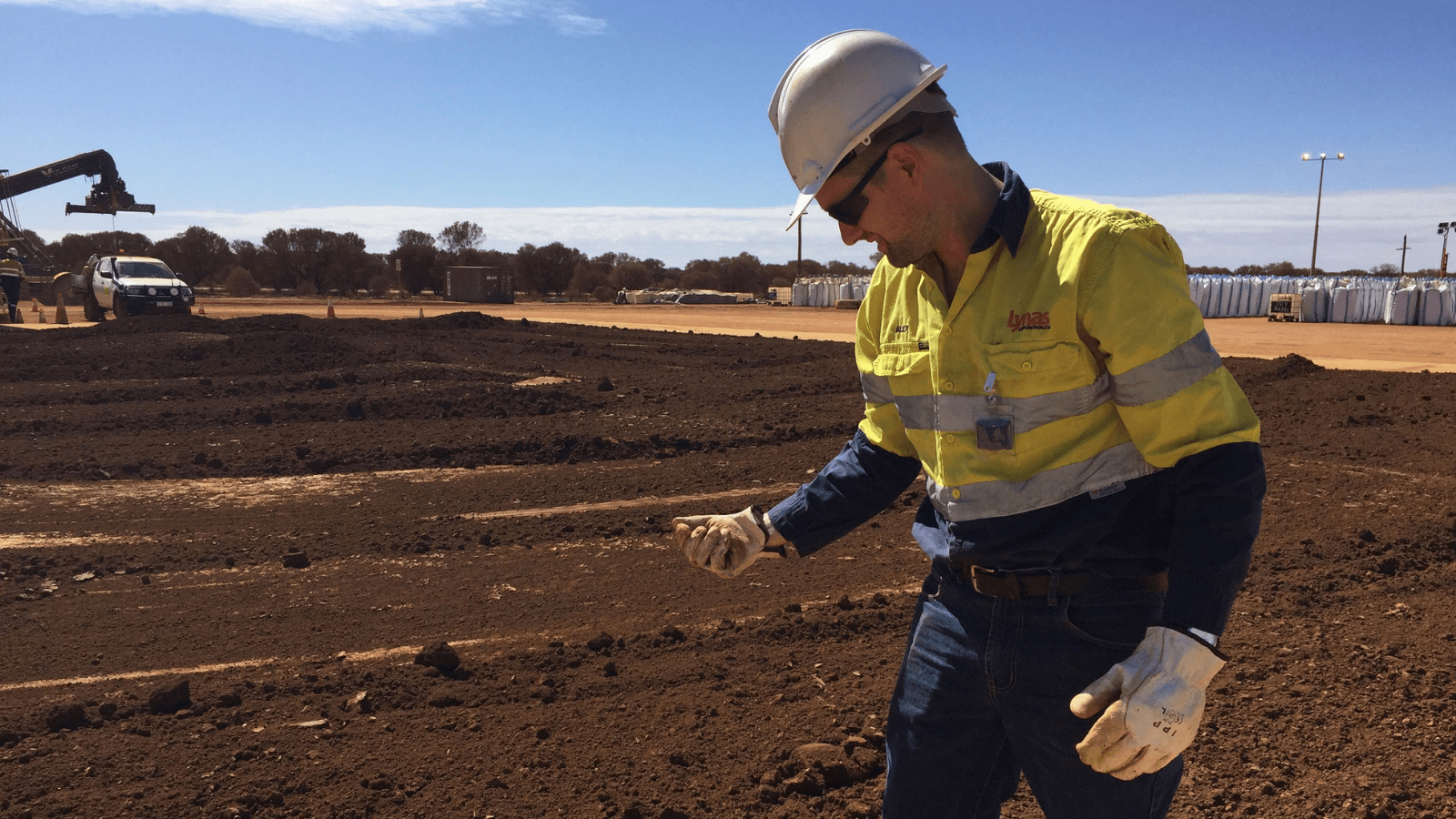A worker picks up a handful of rare earth concentrate left to dry in the sun before it is packed and shipped to Malaysia for processing, at Mt Weld, northeast of Perth