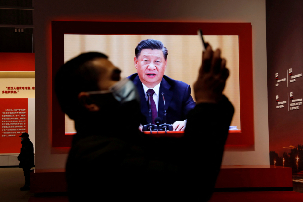 A visitor holds his mobile phone near a screen showing Chinese President Xi Jinping