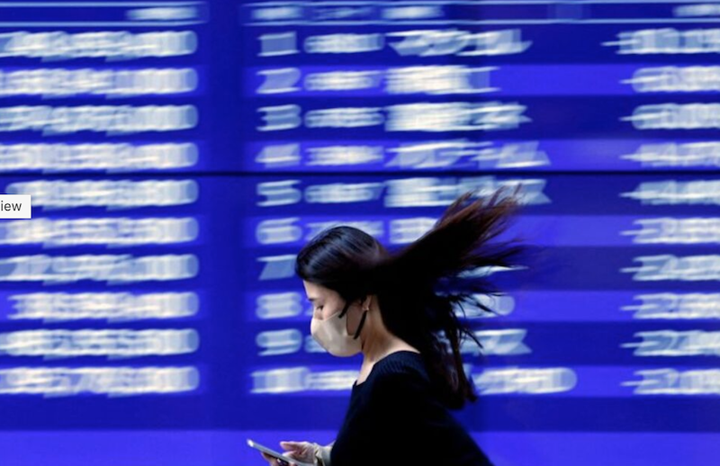 A passerby walks past an electric monitor displaying stock prices outside a bank in Tokyo, Japan. Photo: Reuters.