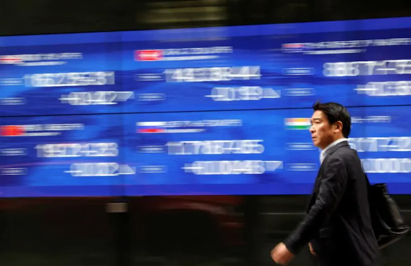 A passerby walks past an electric monitor displaying various countries' stock price index outside a bank in Tokyo, Japan, March 22, 2023. REUTERS/Issei Kato