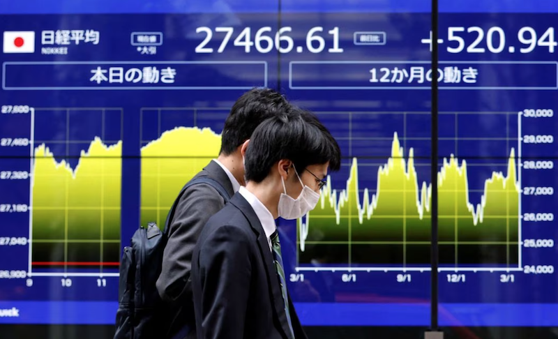 Passersby walk past an electric monitor displaying Japan's Nikkei share average and recent movements outside a bank in Tokyo, Japan, March 22, 2023. REUTERS/Issei Kato