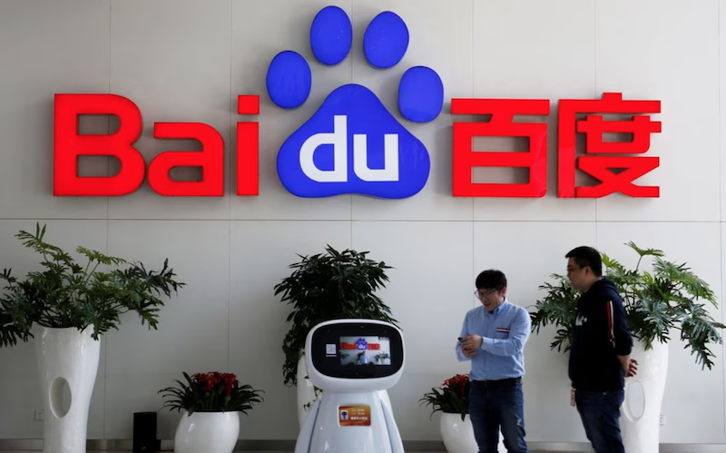Men interact with a Baidu AI robot near the company logo at its headquarters in Beijing, China April 23, 2021. REUTERS/Florence Lo