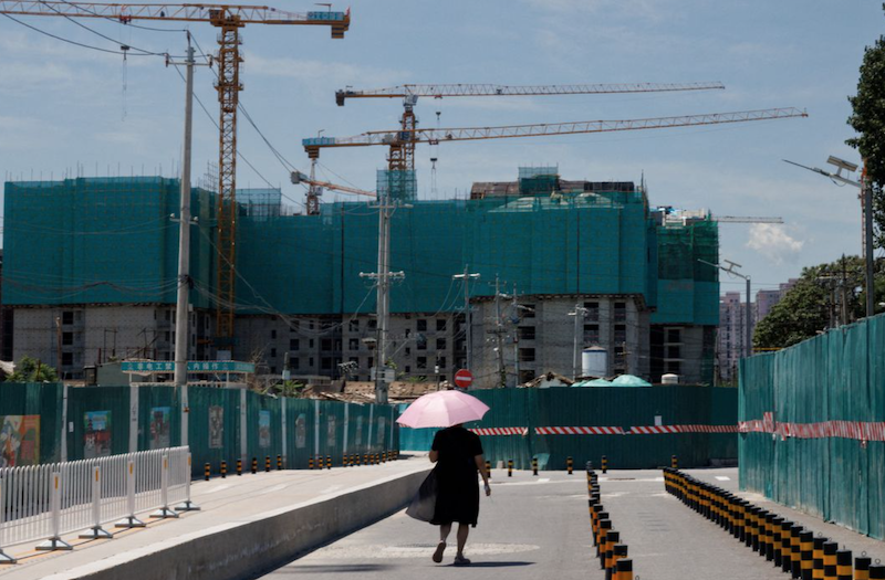 A woman walks near a construction site of apartment buildings in Beijing, China, July 15, 2022. REUTERS/Thomas Peter/File Photo