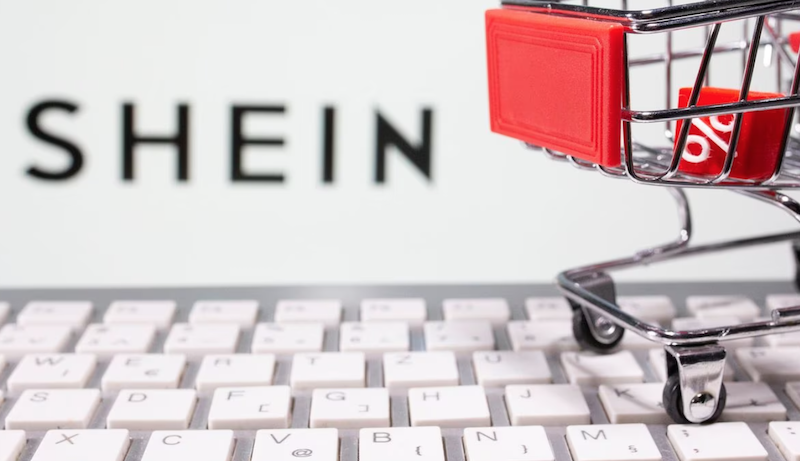 A keyboard and a shopping cart are seen in front of a displayed Shein logo in this illustration