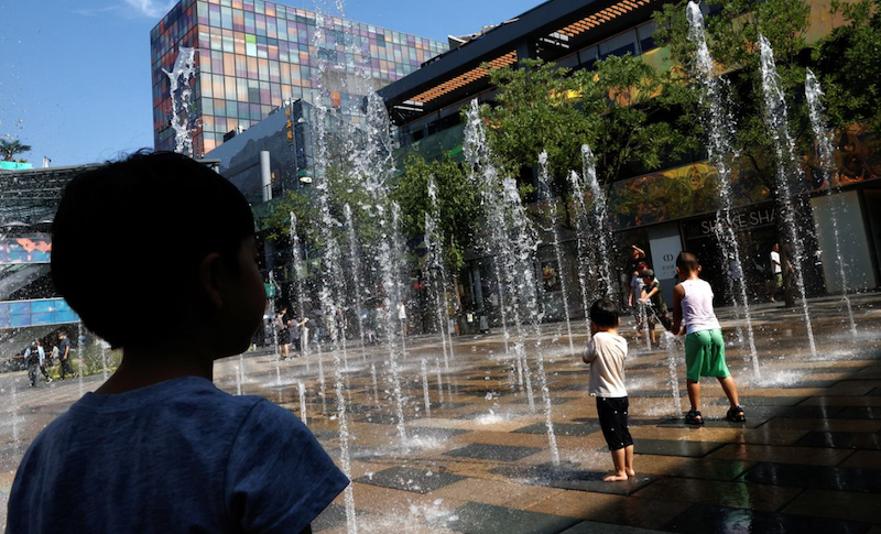 Children cool off in a water fountain amid an orange alert for heatwave, at a shopping area in Beijing, China June 22, 2023. REUTERS/Tingshu Wang