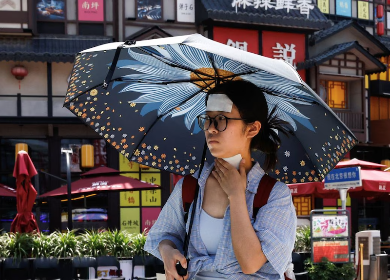 A woman walks with cold patches on her forehead and neck amid a red alert for heatwave in Beijing, China June 23, 2023. REUTERS/Tingshu Wang