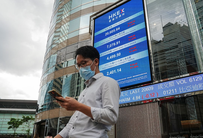 A man walks past a screen displaying the Hang Seng stock index outside Hong Kong Exchanges, in Hong Kong, China July 19, 2022. REUTERS/Lam Yik/File Photo