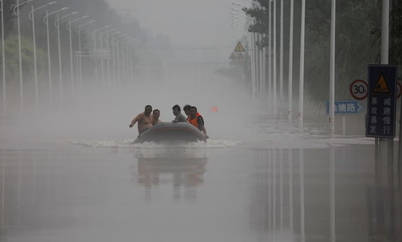 People ride a boat through a flooded road after the rains and floods brought by remnants of Typhoon Doksuri, in Zhuozhou, Hebei province, China August 3, 2023. REUTERS/Tingshu Wang/File Photo