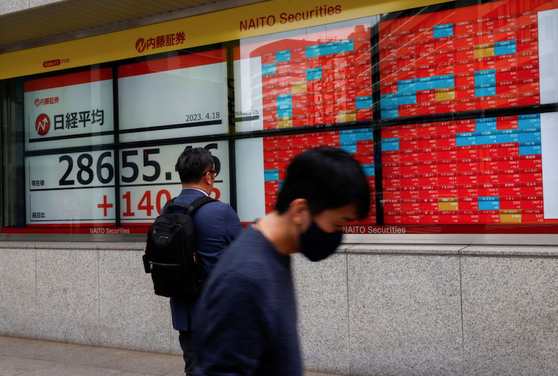 Passersby walk past an electric board displaying Japan's Nikkei share average outside a brokerage in Tokyo, Japan April 18, 2023. REUTERS/Issei Kato