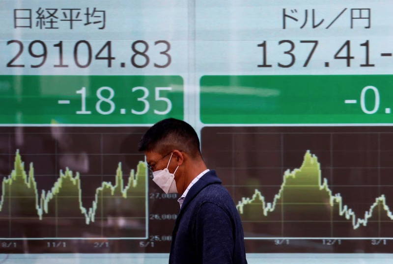 A man walks past an electric monitor displaying Nikkei share average and the Japanese yen exchange rate against the U.S. dollar outside a brokerage in Tokyo, Japan May 2, 2023. REUTERS/Issei Kato Acquire Licensing Rights