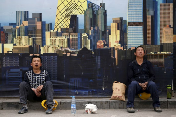 Construction workers take a nap in front of a wall of a construction site during their lunch break in Beijing, China