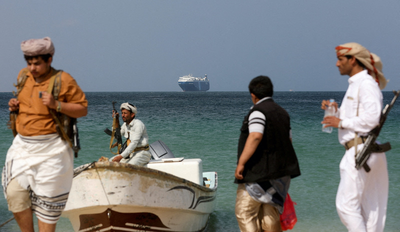 Armed men stand on the beach as the Galaxy Leader commercial ship, seized by Yemen's Houthis last month, is anchored off the coast of al-Salif, Yemen