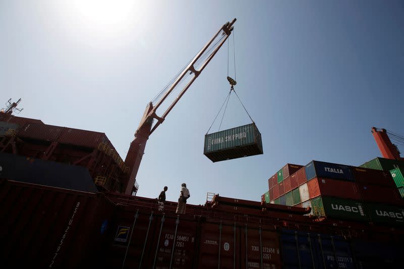 Workers look on as a ship uses its crane to unload containers at a terminal at the Red Sea port of Hodeidah