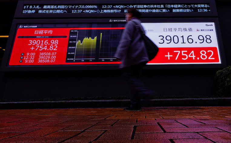 A passerby walks past in front of electronic screens displaying Japan's Nikkei share average, which surged past an all-time record high scaled in December 1989, outside a brokerage in Tokyo, Japan