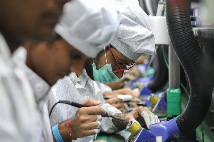 Workers solder wires on printed circuit boards of a mobile handset at Lava International Limited's manufacturing plant in Noida, India