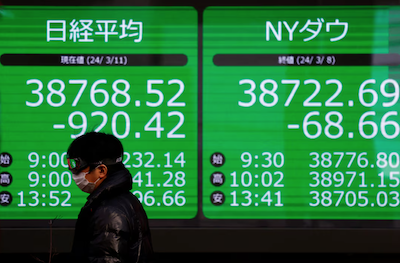 A passerby walks past an electric screen displaying Japan's Nikkei share average and the Dow Jones Industrial Average outside a brokerage in Tokyo, Japan, on March 11, 2024. Photo: Reuters