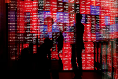 Visitors and electronic screens displaying Japan's Nikkei stock quotation board are reflected on window glasses