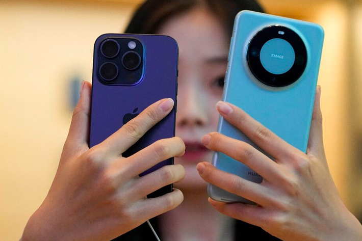 A woman looks at a new iPhone 15 Pro and a Huawei Mate 60 Pro as Apple's new iPhone 15 officially goes on sale across China, at an Apple store in Shanghai, China