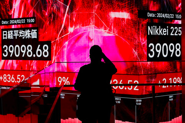 A visitor using his smartphone takes photos of an electronic screen displaying Japan's Nikkei share average, which surged past an all-time record high scaled in December 1989, inside a building in Tokyo