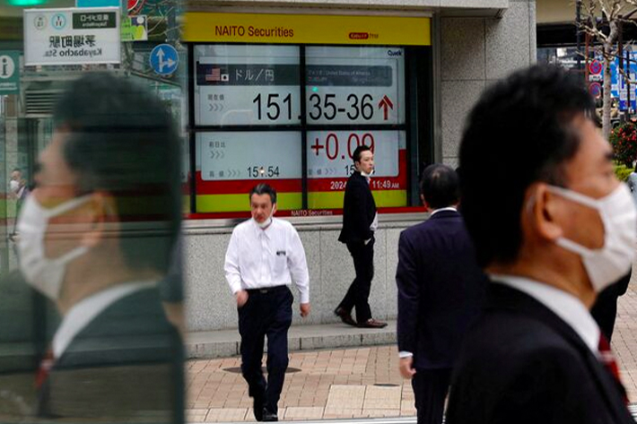 Pedestrians walk past an electric monitor displaying the Japanese yen exchange rate against the U.S. dollar outside a brokerage.