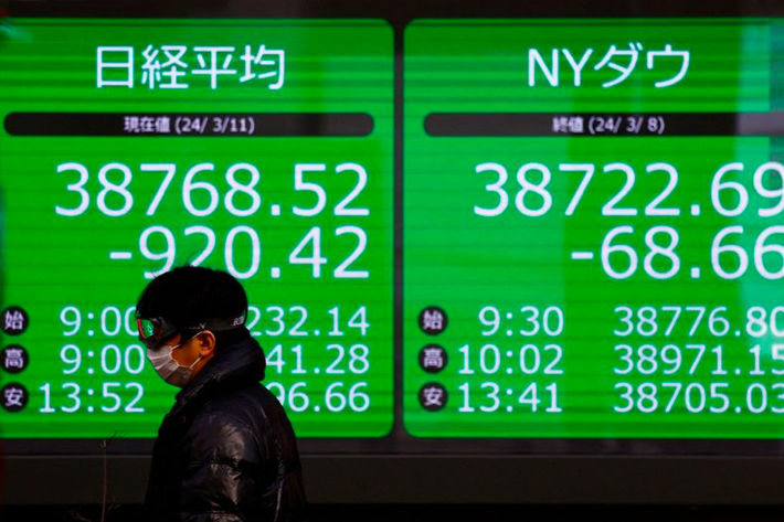 A passerby walks past an electric screen displaying Japan's Nikkei share average and the Dow Jones Industrial Average outside a brokerage in Tokyo.