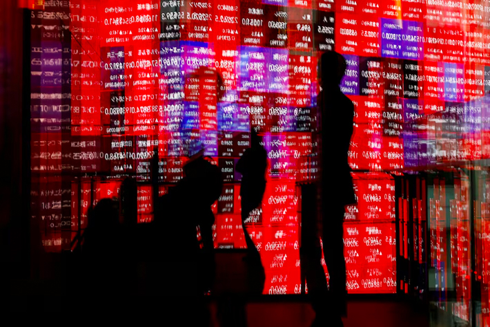 Visitors and electronic screens displaying Japan's Nikkei stock quotation board are reflected on window glasses as the share average surged past an all-time record high in Tokyo.