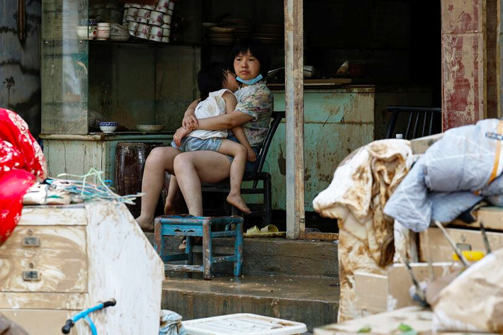 A resident holds a child as she sits at a shop after a flood following heavy rainfall in Pingjiang county of Yueyang, Hunan province, China