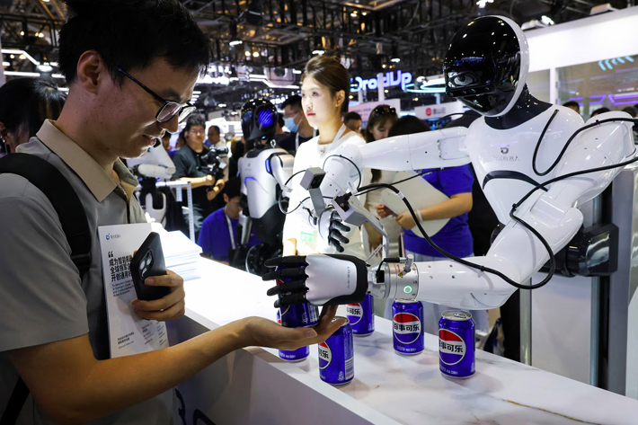 A person receives a can of soda from a humanoid robot at an Agibot booth during the World Artificial Intelligence Conference in Shanghai, China.